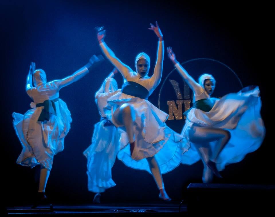 ILF dancers in white costumes mid-leap under blue stage light